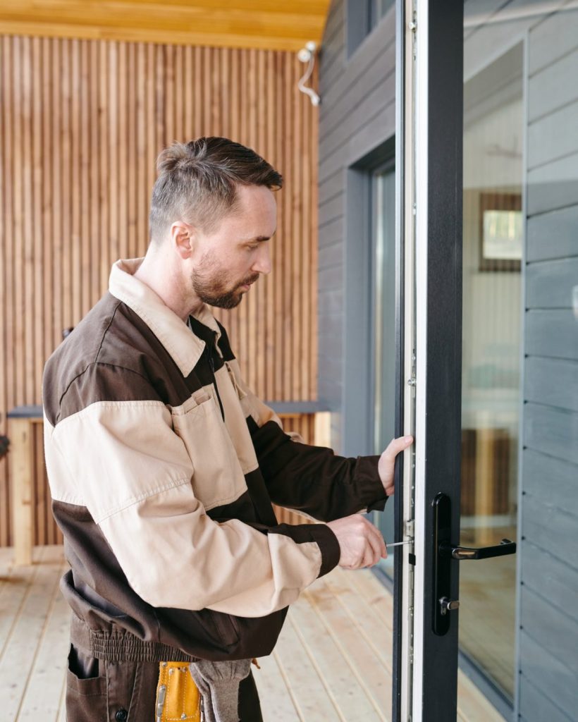 Young repairman fixing lock in large transparent door